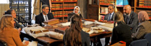 Guests and staff sitting around a table in the Royal Courts of Justice Library. Old and rare books are laid out onto the table.