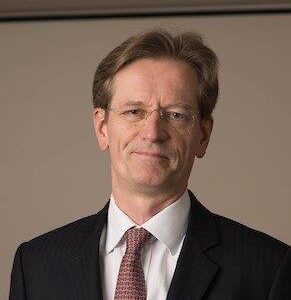 Profile photo of Justice Henshaw wearing a black suit and red tie. The judge is smiling at the camera.