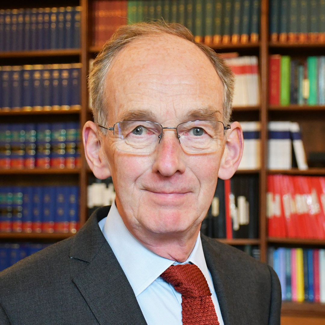 Sir Andrew McFarlane, in front of bookshelves, wearing a suit and tie