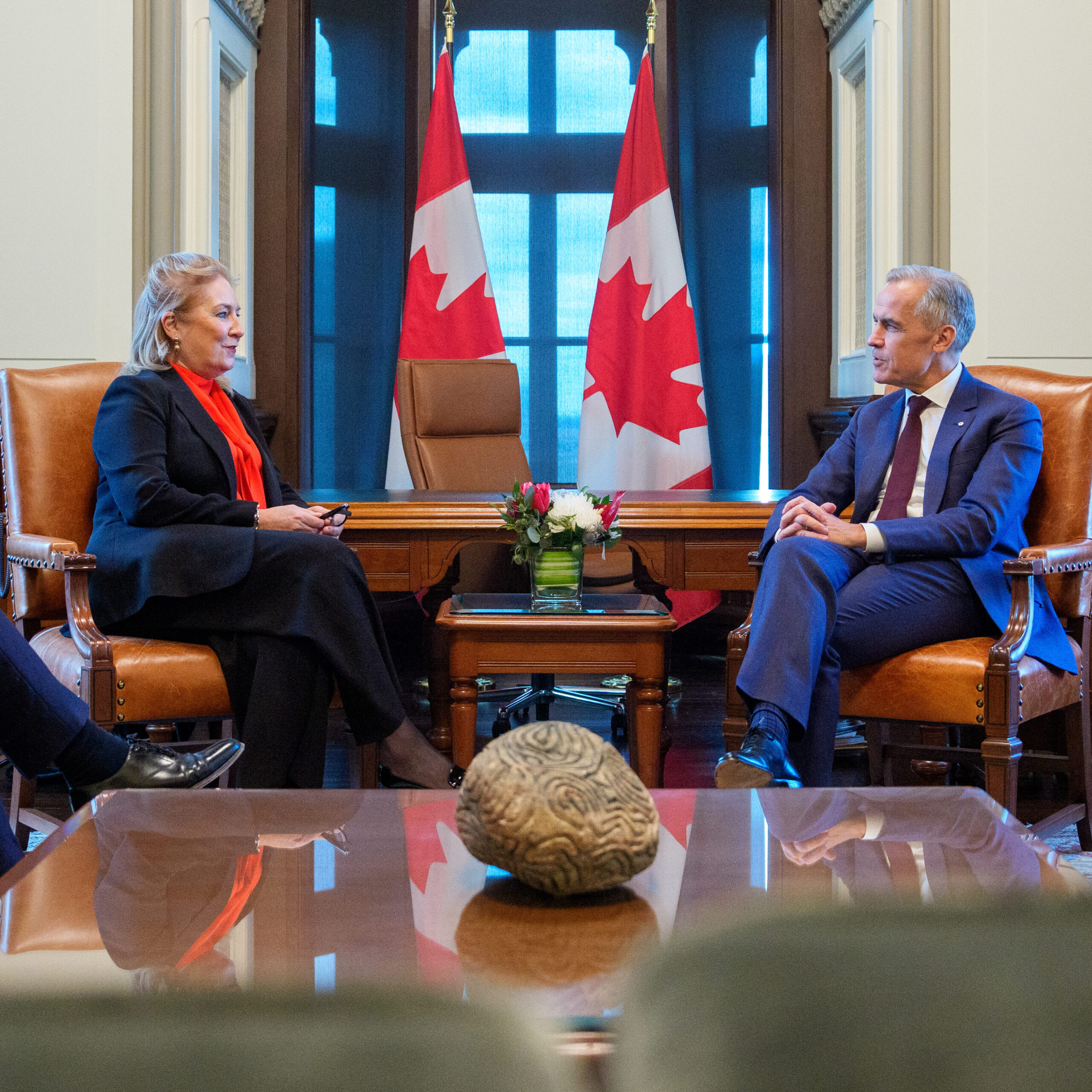 The Lady Chief Justice sits left and the Prime Minister of Canada, Mark Carney sits right between a small desk surrounded by Canadian flags.